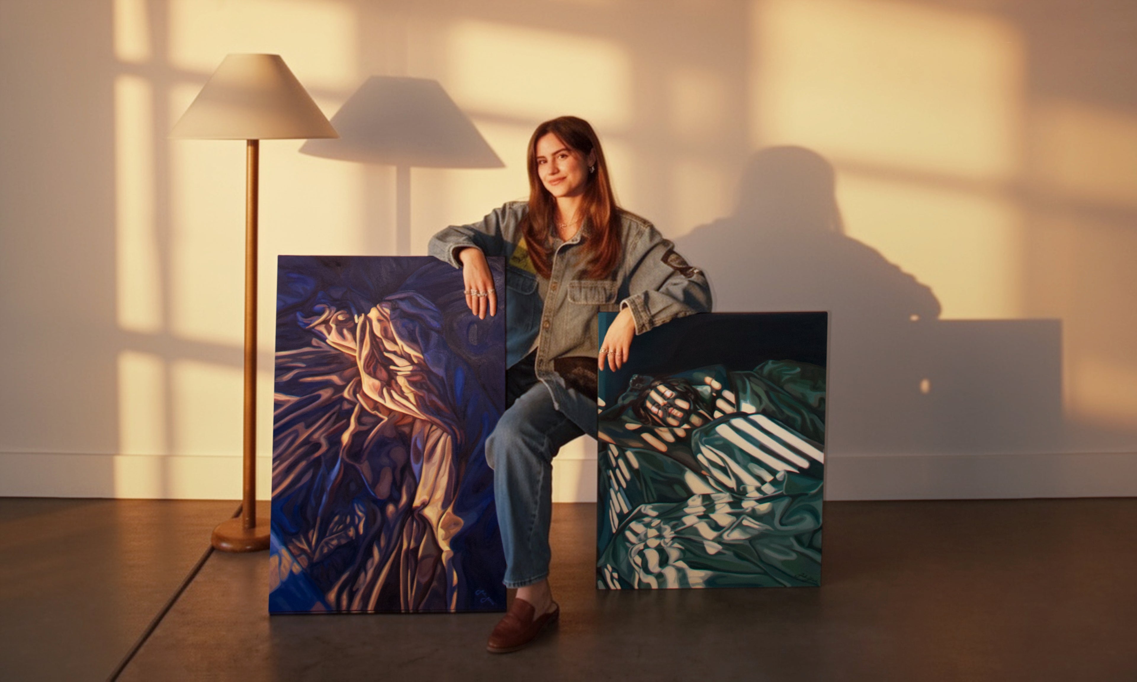 Woman sitting between two large oil paintings on canvases in a room with warm lighting.